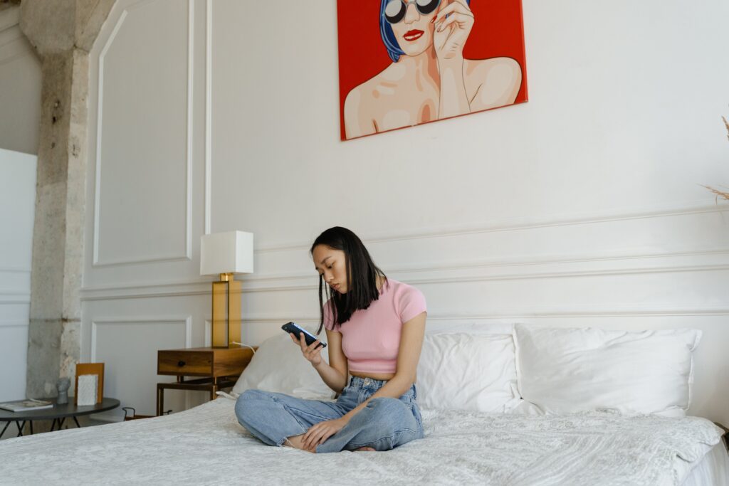 A woman sitting on a bed while using smartphone to correct her credit score