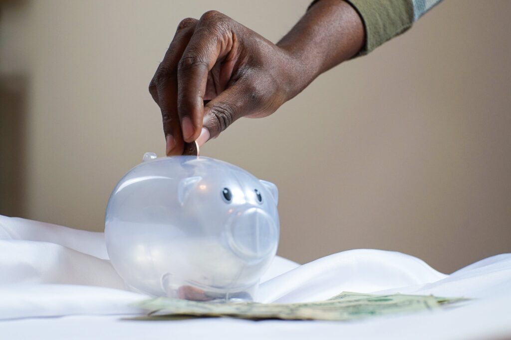 Person putting coin in a piggy bank, saving which a good money habit