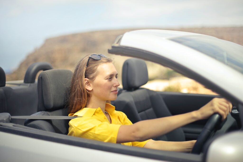 Woman in yellow shirt driving a silver car she bought with an auto loan